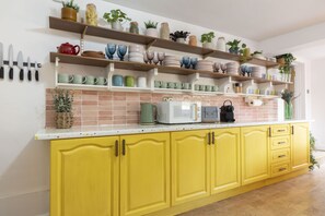 Une cuisine avec des meubles de couleur jaune, des plans de travail blancs, et divers ustensiles de cuisine et plantes disposés sur des étagères.