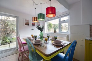 Een eethoek met een houten tafel voor vier personen, kleurrijke stoelen en hanglampen.
