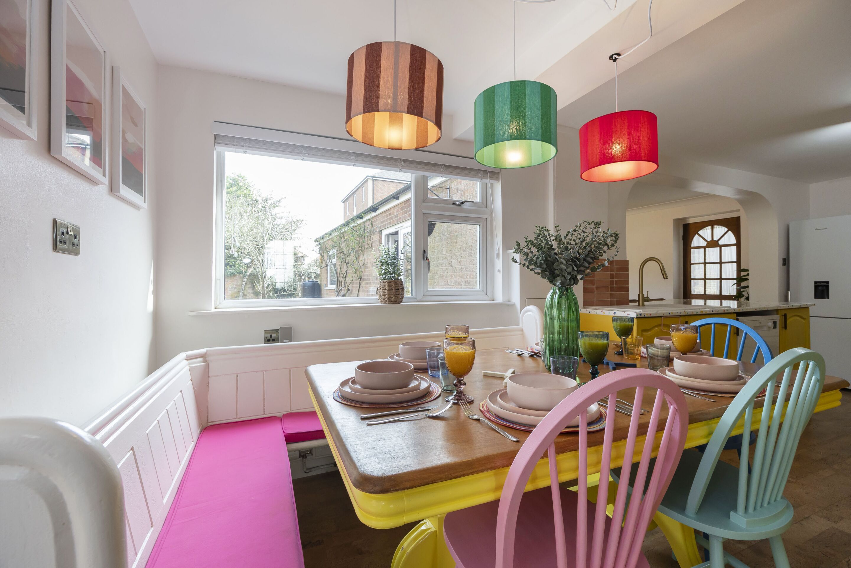 A dining area with a wooden table set for four, colorful chairs, and pendant lights.
