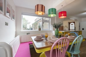 Un coin repas avec une table en bois dressée pour quatre personnes, des chaises colorées et des lampes suspendues.
