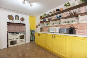 Une cuisine avec des placards jaunes, une cuisinière, un four à micro-ondes et divers ustensiles de cuisine rangés sur des étagères.