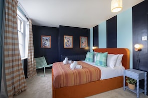Une chambre à coucher avec un lit, une table de chevet, une chaise et des œuvres d’art accrochées au mur.