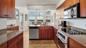 A modern kitchen with wooden cabinets, granite countertops, a dishwasher, a stove, and a microwave. - Top Floor Waterfront Villa on Private Island (Lago Vista)