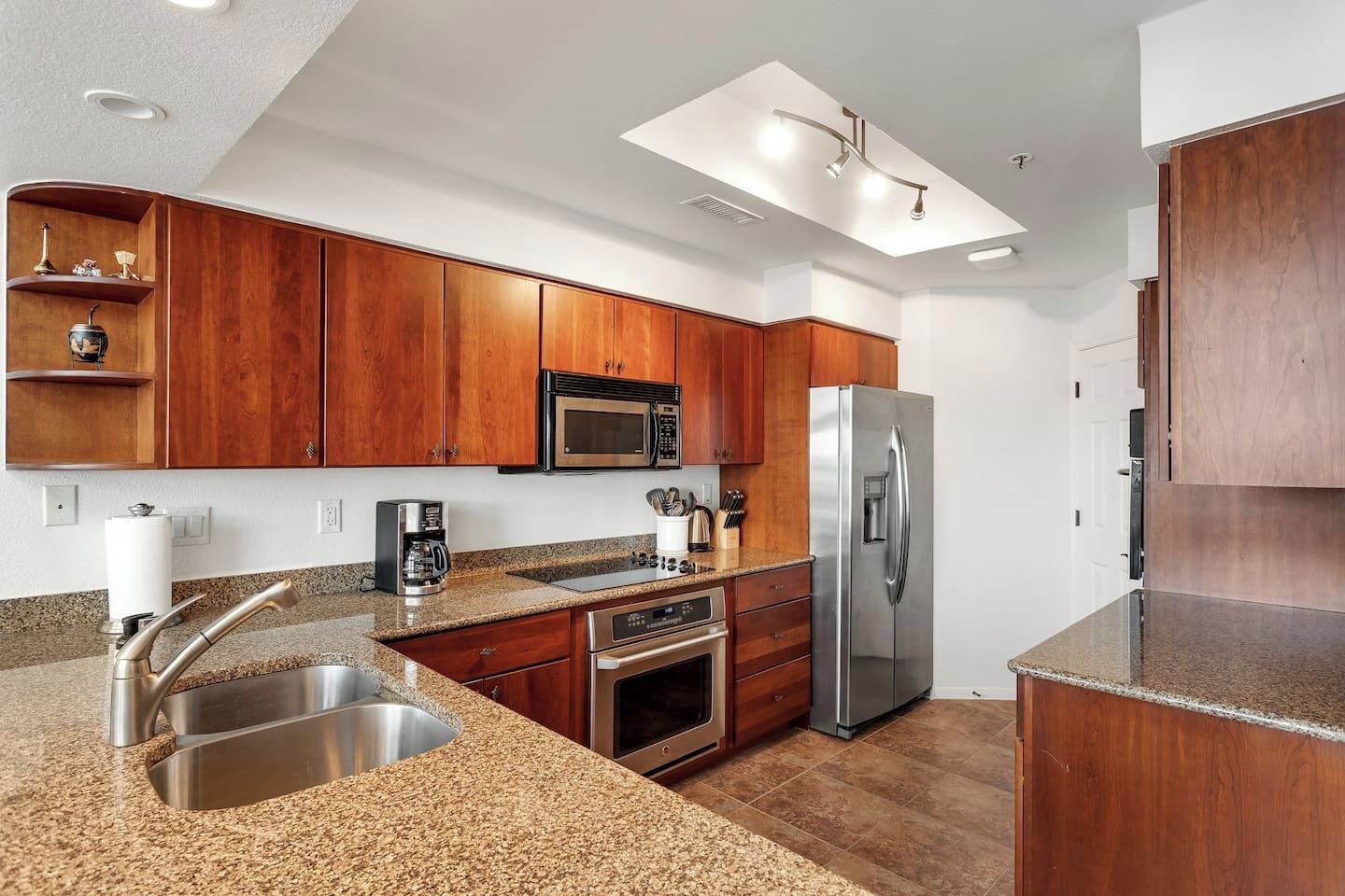 A modern kitchen with wooden cabinets, stainless steel appliances, granite countertops, and a built-in oven.