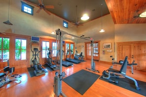 A gym with exercise equipment, wooden floors, and large windows. - Hollows Villa with Panoramic Lake Views / 4 Pools (Jonestown)