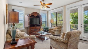 A living room with a ceiling fan, a television, patterned armchairs, a coffee table, and a lamp. - Lovely Villa in the Hollows, Lake View, 4 Pools (Jonestown)