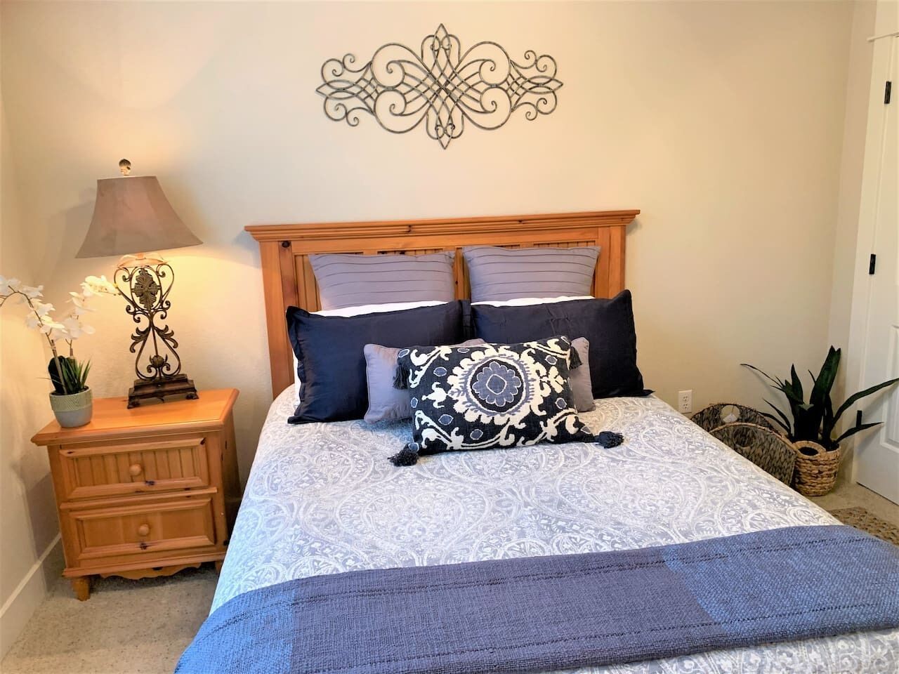 A neatly arranged bedroom with a bed, bedside tables, a decorative wall piece, and potted plants.