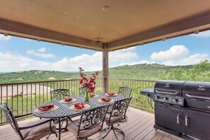 A covered outdoor patio with a table set for dining, a grill, and a scenic view of green hills. - Home in The Hollows, Panoramic View, All Amenities (Jonestown)