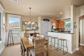 A kitchen with a dining area, wooden cabinets, a chandelier, and a view of the outdoors. - Stunning Lake Travis Views, All Hollows Amenities (Leander)