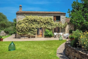 A stone house with a tiled roof, a covered patio, and a garden with potted plants and outdoor furniture.