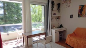 Una habitación con balcón, una silla blanca, una mesa, un sofá y un radiador.