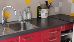 Una cocina con gabinetes rojos, un lavamanos de acero inoxidable y una encimera con utensilios de cocina.