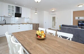 A modern kitchen with white cabinets, a wooden dining table, and a fruit bowl. - Cozy home in Makarska (Makarska)