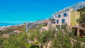 Una proprietà collinare con un edificio in pietra, una zona esterna coperta e vista sul mare.