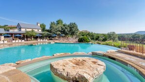 Ein Pool mit Felsen, Liegestühlen und einem Gebäude mit Satteldach.