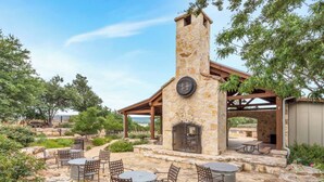 A stone-built outdoor kitchen with a chimney, surrounded by stone seating and a pergola.