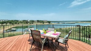 A deck with a table and chairs overlooking a body of water and distant landscape. - Lake Oaks Landing-Sunset Lake Views-Lago Amenities (Lago Vista)