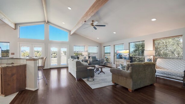 A spacious living area with a kitchen, large windows, and a ceiling fan. - Lake Oaks Landing-Sunset Lake Views-Lago Amenities (Lago Vista)