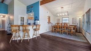 A spacious dining area with wooden chairs and a large table, a kitchen with modern appliances, and a loft bedroom with a sloped ceiling. - Lake Oaks Landing-Sunset Lake Views-Lago Amenities (Lago Vista)