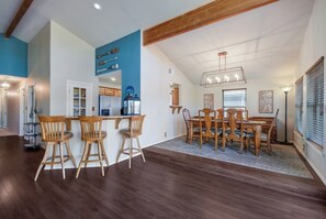 A spacious dining area with wooden chairs and a large table, a kitchen with modern appliances, and a loft bedroom with a sloped ceiling. - Lake Oaks Landing-Sunset Lake Views-Lago Amenities (Lago Vista)