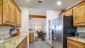 A kitchen with wooden cabinets, a stainless steel refrigerator, and a granite countertop. - Lake Oaks Landing-Sunset Lake Views-Lago Amenities (Lago Vista)