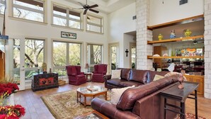 A spacious living room with a high ceiling, large windows, and a fireplace. - Hill Country Estate | 49 Acres | Pool | Game Room | Great Deals! (Lago Vista)