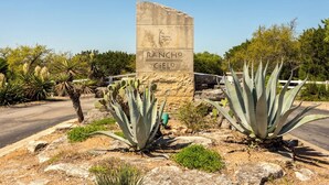 A stone sign with 'Rancho Cielo' written on it, surrounded by agave plants and desert vegetation. - Hill Country Estate | 49 Acres | Pool | Game Room | Great Deals! (Lago Vista)
