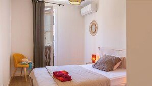 Ein Schlafzimmer mit einem Bett, einem Sessel, einem Nachttisch mit Lampe und einer Klimaanlage an der Wand.