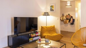 Ein modernes Wohnzimmer mit Flachbildfernseher, einer Couch, einem Couchtisch und einer Lampe.