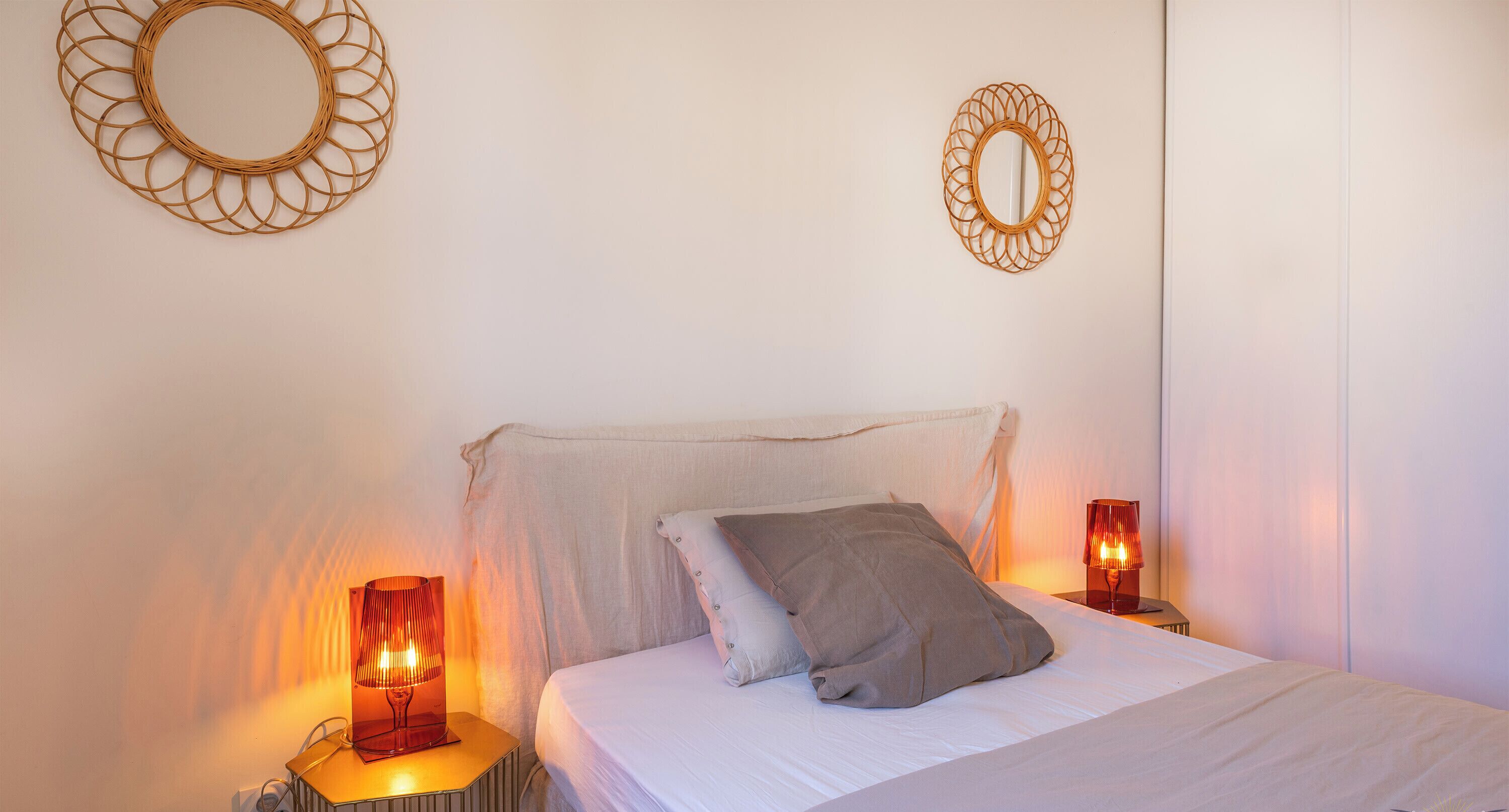 A bedroom with a bed, two bedside lamps, and two wall-mounted mirrors.