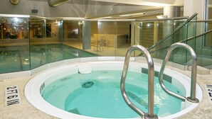 Piscina interna com água cristalina, cercada por paredes de vidro e guarda-corpos de metal.