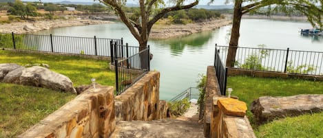 Una escalera de piedra que desciende hasta la orilla de un río, con una valla metálica y árboles.