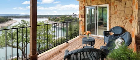 A balcony with a view of a river and distant buildings, a ceiling fan, and outdoor furniture.