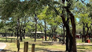 A park with trees, a playground, and a dirt path. - The Lazy Lakehouse - All LVPOA Amenities Available (Lago Vista)