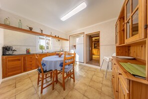 A kitchen with wooden cabinets, a dining table with chairs, a refrigerator, and a coffee machine. - Villa del la Vilar - Two Bedroom Villa, Sleeps 4 (Mallorca)