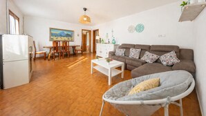 Ett vardagsrum med en soffa, ett matbord, stolar, ett vitt soffbord, en hängande lampa och en liten balkong med en stol.