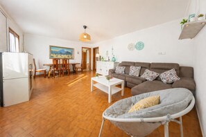 A living room with a sofa, a dining table, chairs, a white coffee table, a hanging light fixture, and a small balcony with a chair. - Villa del la Vilar - Two Bedroom Villa, Sleeps 4 (Mallorca)