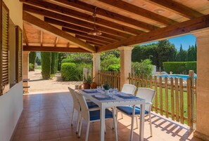 An outdoor patio with a wooden pergola, a table set for dining, and a pool in the background. - Villa del la Vilar - Two Bedroom Villa, Sleeps 4 (Mallorca)