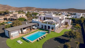 En moderne villa med swimmingpool, udendørs siddepladser og udsigt over det omkringliggende kvarter.