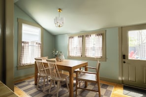 A dining area with a wooden table and chairs, a chandelier, and windows with curtains. - The Single Barrel - Deck, Fire Pit, Hot Tub, Games (Louisville)