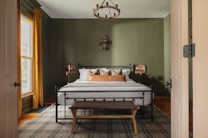 A bedroom with a bed, bedside lamps, a bench, a chandelier, and a wall-mounted light fixture. - The Single Barrel - Deck, Fire Pit, Hot Tub, Games (Louisville)