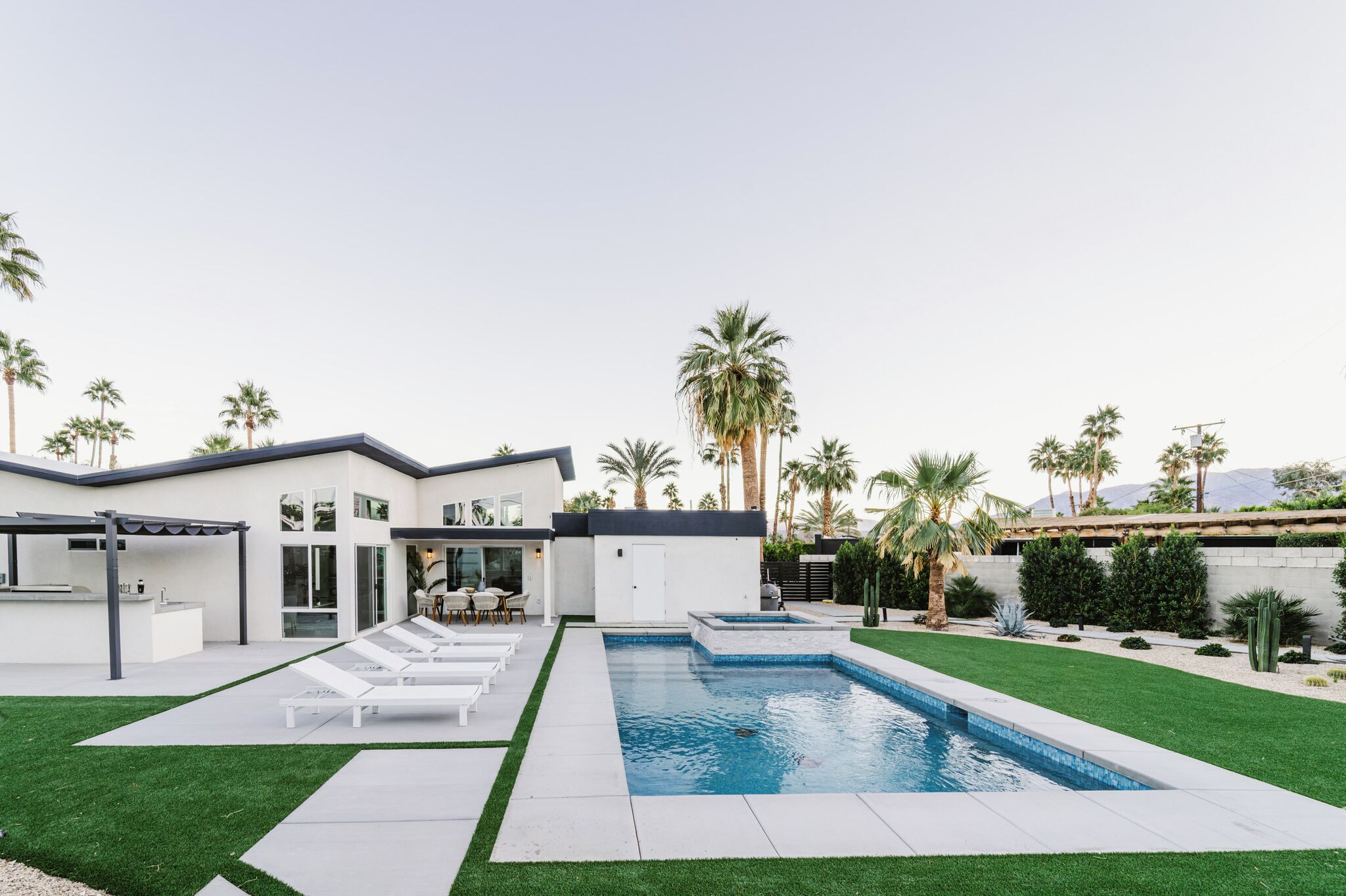 Une maison moderne dotée d’une piscine, d’un patio avec des chaises longues et d’un jardin bien entretenu.