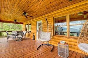 Eine Holzhütte mit einer Terrasse, einem Esstisch mit Stühlen, einem Hängesessel und einem kleinen runden Tisch mit einer Kerze.