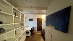 A compact room with a white desk, shelves, a bed with a colorful blanket, and a large abstract painting on the wall. - Private Writers Room at SaddleRock Ranch in Heart of Sedona (Sedona)