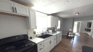 Una cocina con gabinetes blancos, una estufa negra, un lavamanos y una zona de comedor con mesa y sillas.