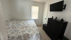 Un dormitorio con cama, cómoda y televisor montado en la pared.