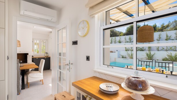 A modern kitchen with a wooden countertop, a cake on a stand, and a view of a swimming pool through large windows. - Villa Verde Ra anj With Heated Pool (Rogoznica)