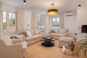 Een ruime woonkamer met een grote zithoek, een salontafel en een kroonluchter.