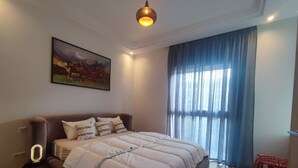 Ein Schlafzimmer mit einem großen Bett, einer Nachttischlampe, einem Gemälde und einem Fenster mit Vorhängen.