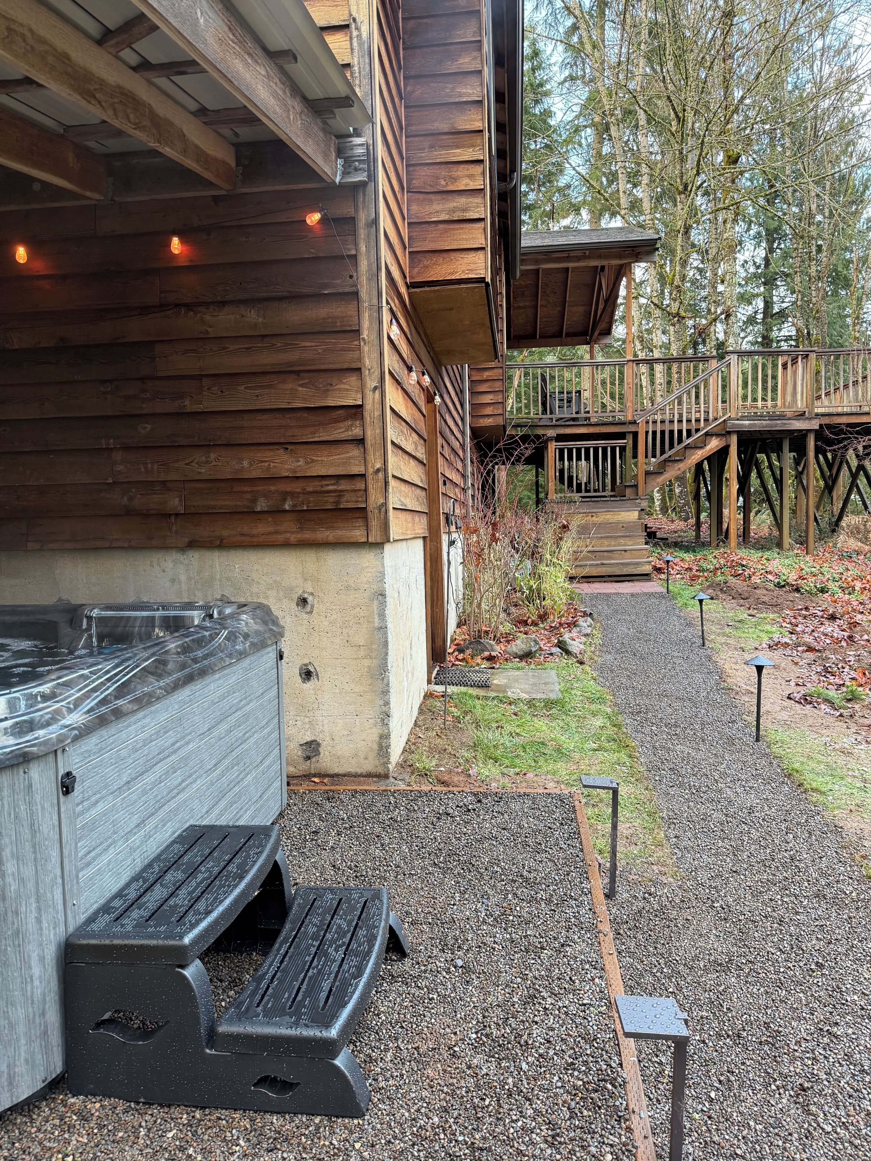 En træbygning med boblebad, terrasse og grussti.